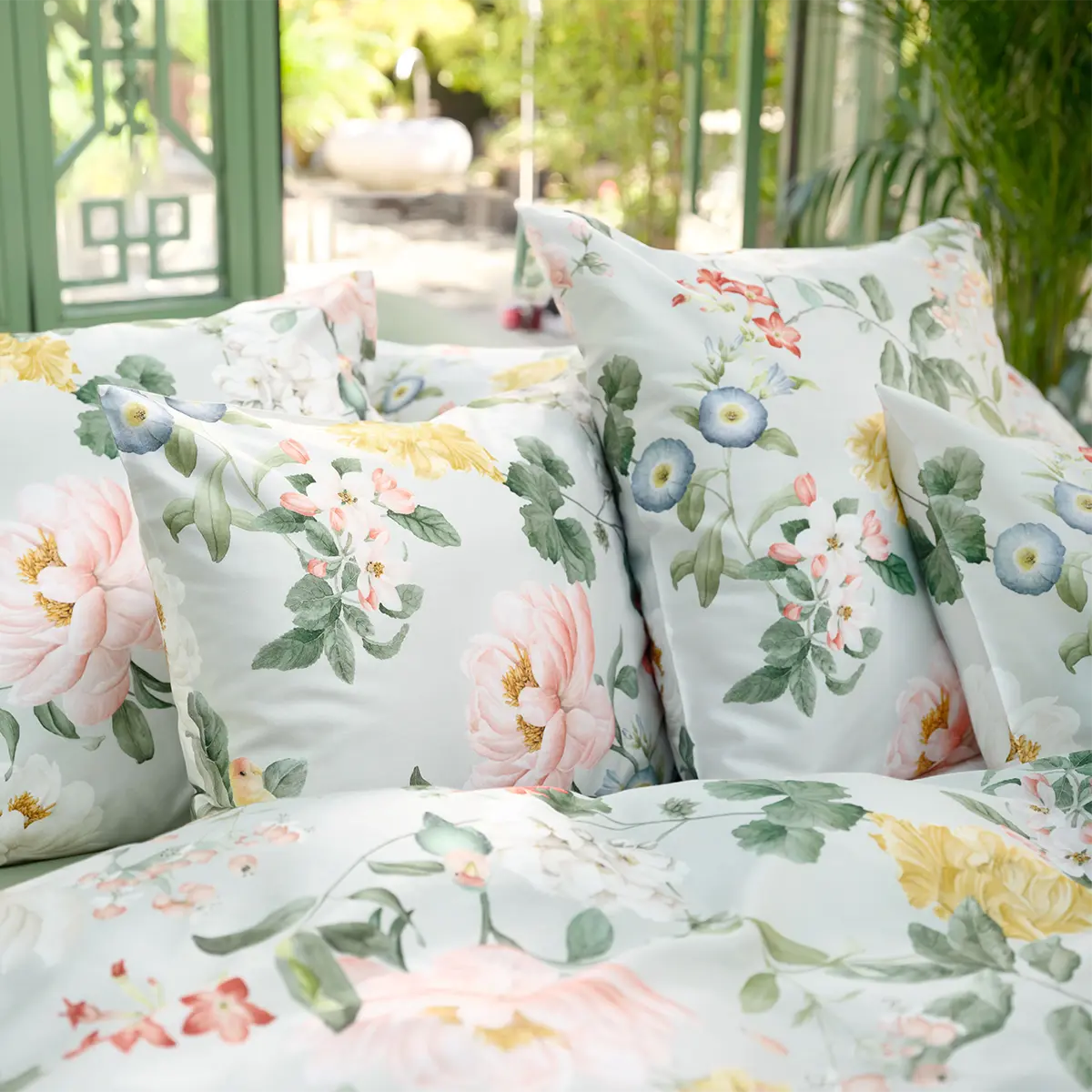 Bettwäsche Artemis mit Blumenmuster und grünen Kissenbezügen, im Garten arrangiert.
