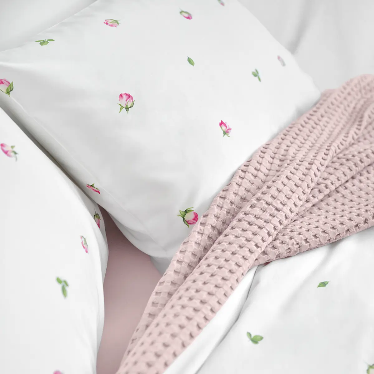 Detailansicht der Jeunesse-Bettwäsche mit zarten Blüten Nahaufnahme der Jeunesse-Bettwäsche, die mit kleinen rosa Blüten und grünen Blättern verziert ist, kombiniert mit einer weichen, rosa Decke.
