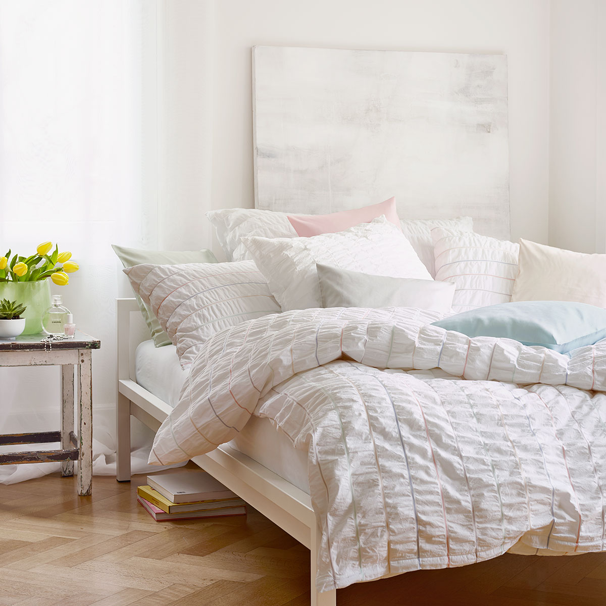 Ein helles Schlafzimmer, das Bett ist mit der Nelson Bettwäsche in einem feinen Streifenmuster in Pastellfarben bezogen.