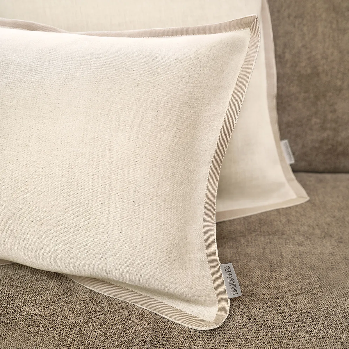 Schlossberg Zierkissen Solene Sand – Hochwertiges Design in sanftem Beige Detailaufnahme von zwei Schlossberg Zierkissen Solene Sand auf einem beigen Sofa. Die feine Struktur des Stoffes, kombiniert mit einer eleganten Paspelierung, verleiht den Kissen eine edle und natürliche Optik – perfekt für stilvolle Wohnräume.