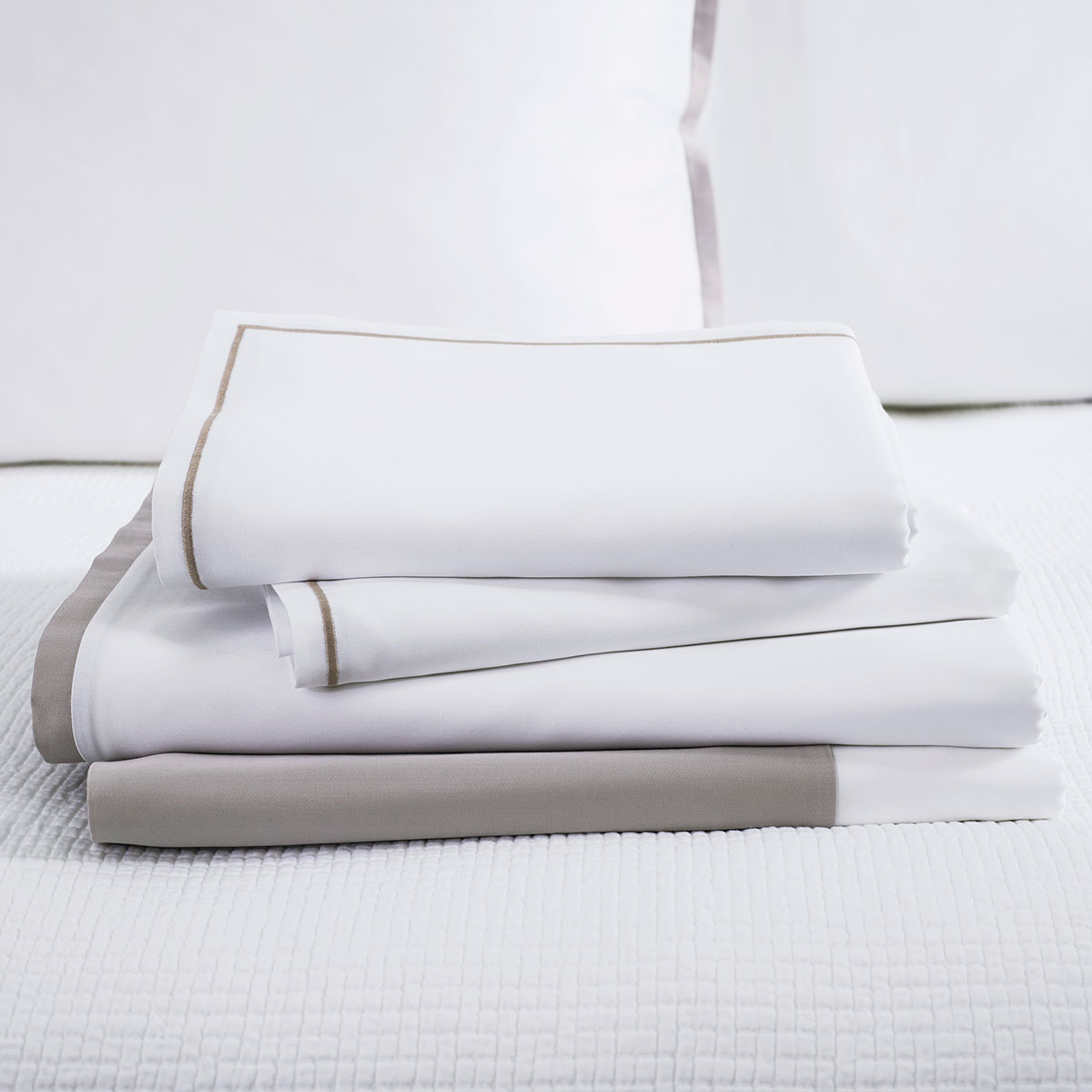 Stapel weisse Bettwäsche Clark mit hellem Rand Ein Stapel der Bettwäsche Clark in weiss mit hellem Rand, ordentlich auf einem Bett drapiert.