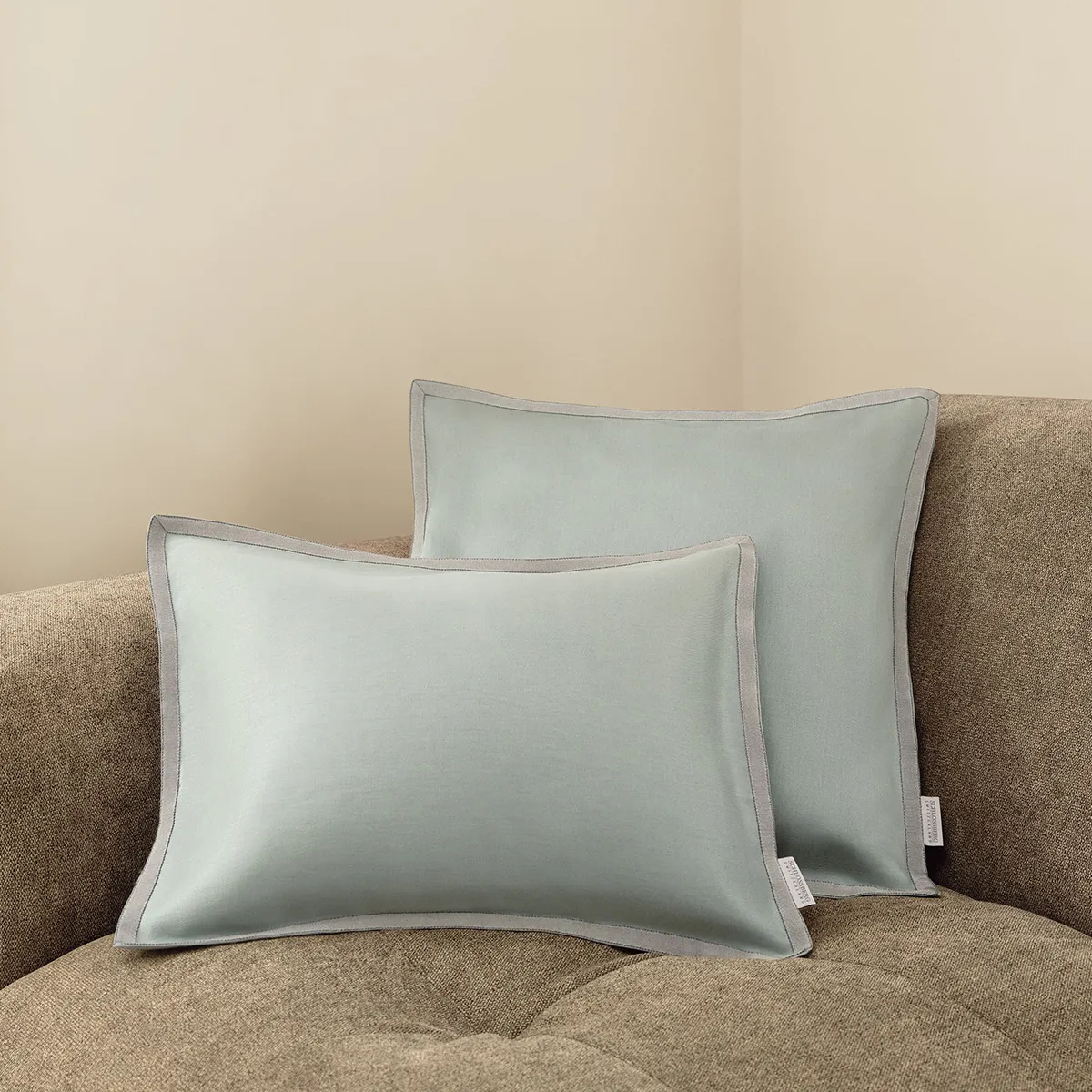 chlossberg Zierkissen Solene in Sage – Zeitlose Eleganz in sanftem Grün Zwei Schlossberg Zierkissen Solene in Sage auf einem beigen Sofa. Das edle Design in sanftem Salbeigrün mit kontrastierender Paspelierung sorgt für eine harmonische und stilvolle Wohnatmosphäre.