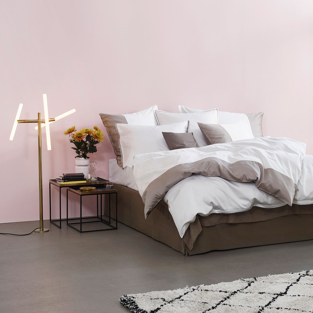 Bettwäsche Allen im stilvollen Schlafzimmer Modernes Schlafzimmer mit weisser und grauer Bettwäsche, Beistelltisch mit Blumen und Büchern, rosa Wand, grauem Boden und weissem Teppich.