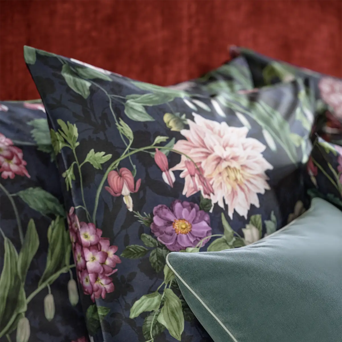Nahaufnahme eines Kopfkissens mit dem dunkelblauen floralen Muster der Ophelia Bettwäsche, ergänzt durch ein grünes Zierkissen.