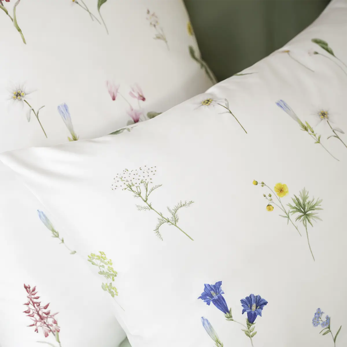 Nahaufnahme von Kopfkissen, die Teil der weissen Bettwäsche "Flurina" mit einem dezenten Blumenmuster sind.