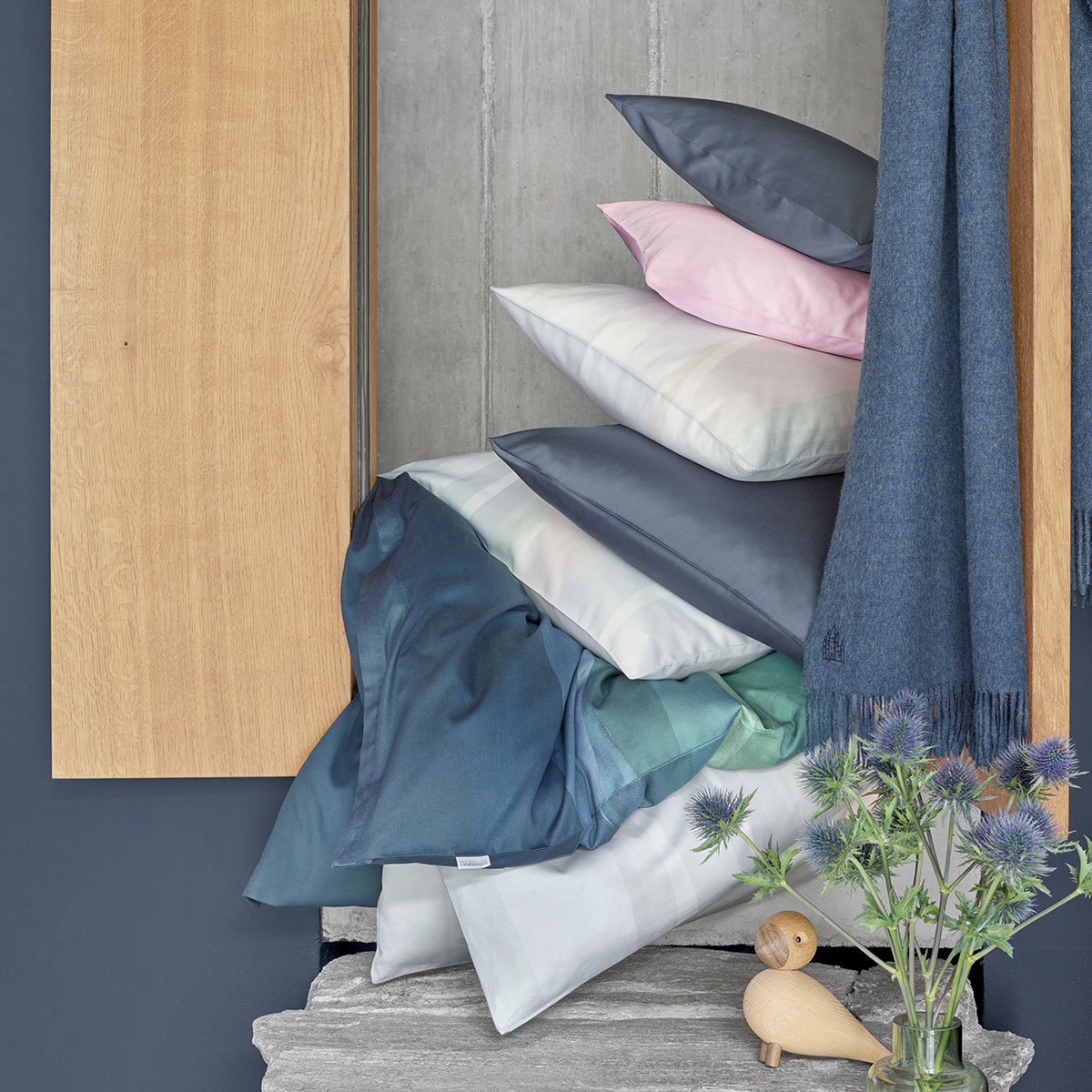 Stapel der Bettwäsche Manoa mit verschiedenen Kissen Bettwäsche Manoa, kunstvoll gestapelt mit Kissen und Textilien, um eine stilvolle und farbenfrohe Kombination zu zeigen.