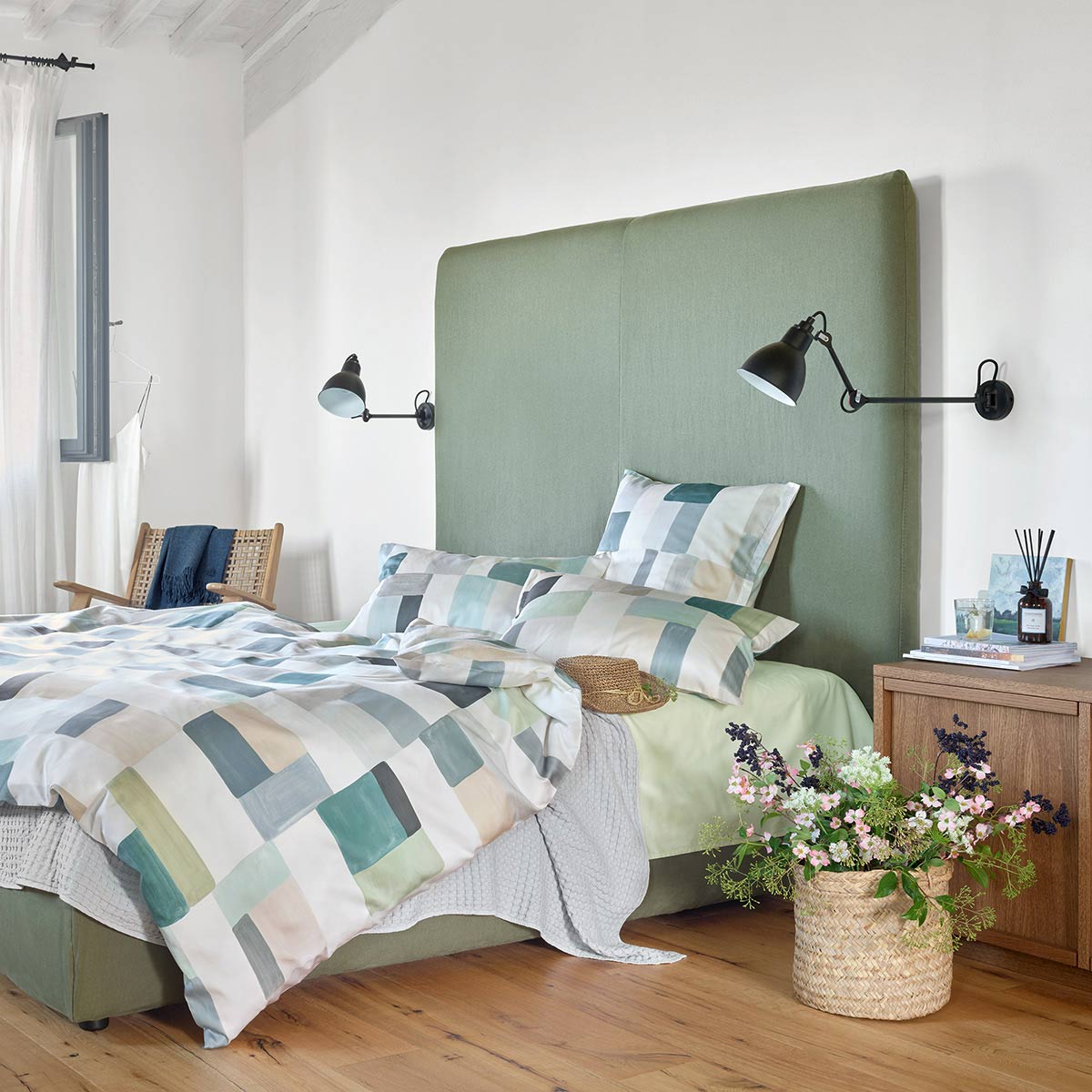 Schlafzimmer mit einem Bett, das mit der Mika Bettwäsche in geometrischem Design bezogen ist, daneben ein Nachttisch mit Blumen.
