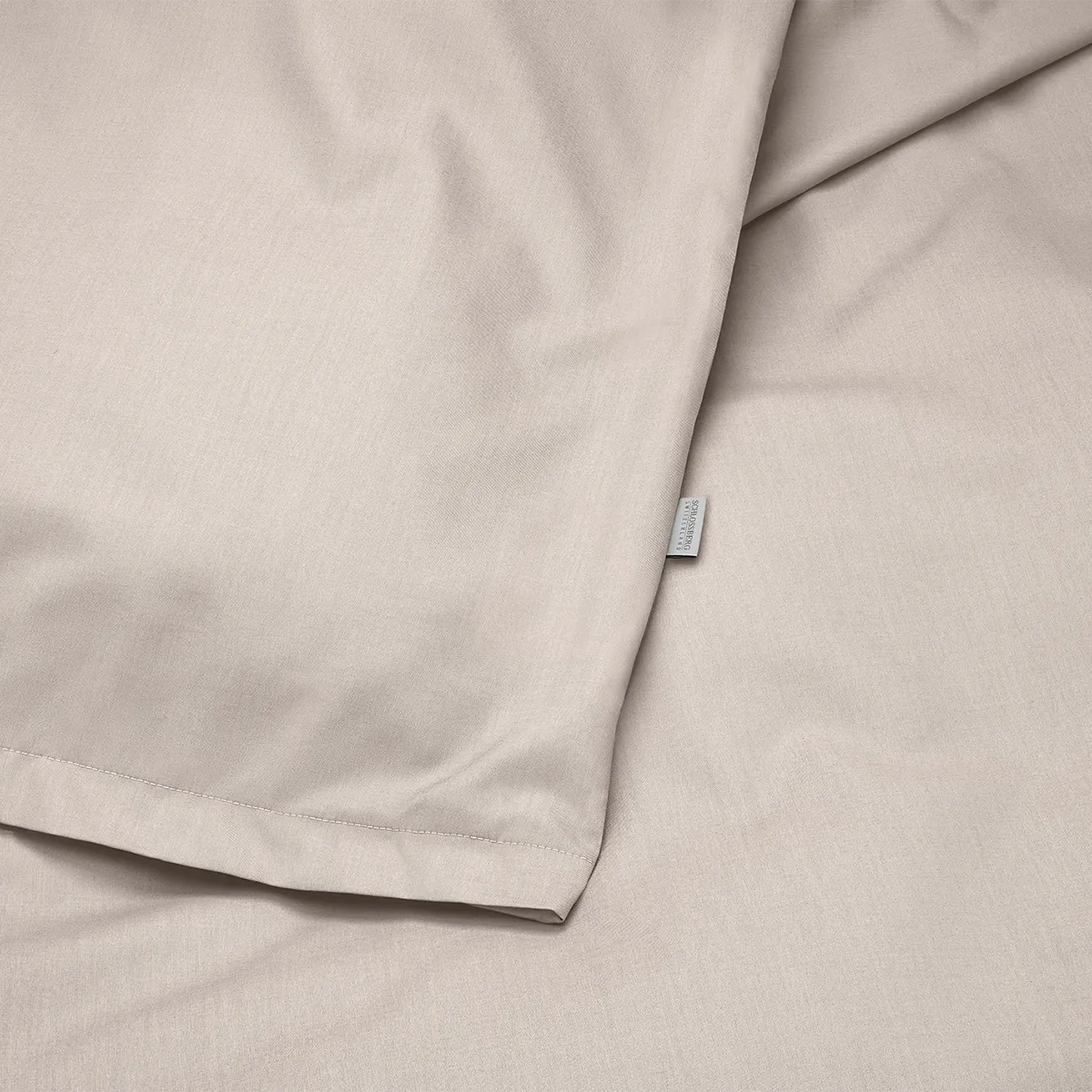 Schlossberg Bettwäsche Ben Sand – Stoffdetail Nahaufnahme der Schlossberg Bettwäsche Ben in der Farbe Sand. Der hochwertige Stoff präsentiert sich in einer feinen, natürlichen Textur mit dezenter Webstruktur und einem kleinen Schlossberg-Label.
