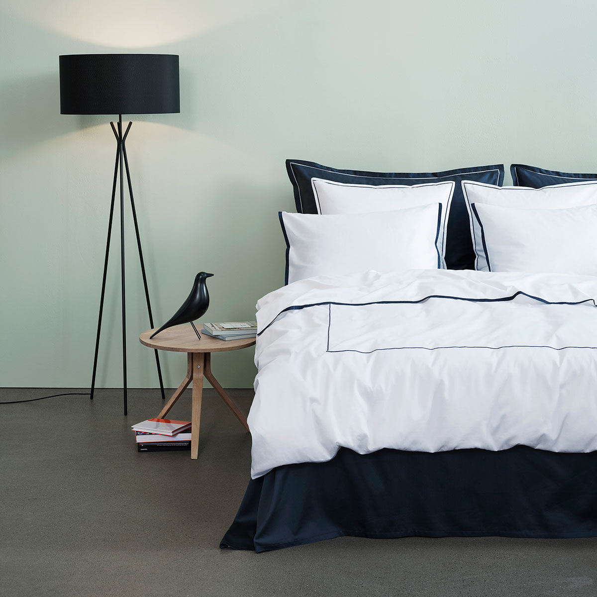 Modernes Schlafzimmer mit Bettwäsche Clark in dunkelblau und weiss Ein modernes Schlafzimmer mit einem Bett, das mit der dunkelblauen und weissen Bettwäsche Clark bezogen ist. Ein stilvolles Nachttischchen und eine Stehlampe runden das Bild ab.