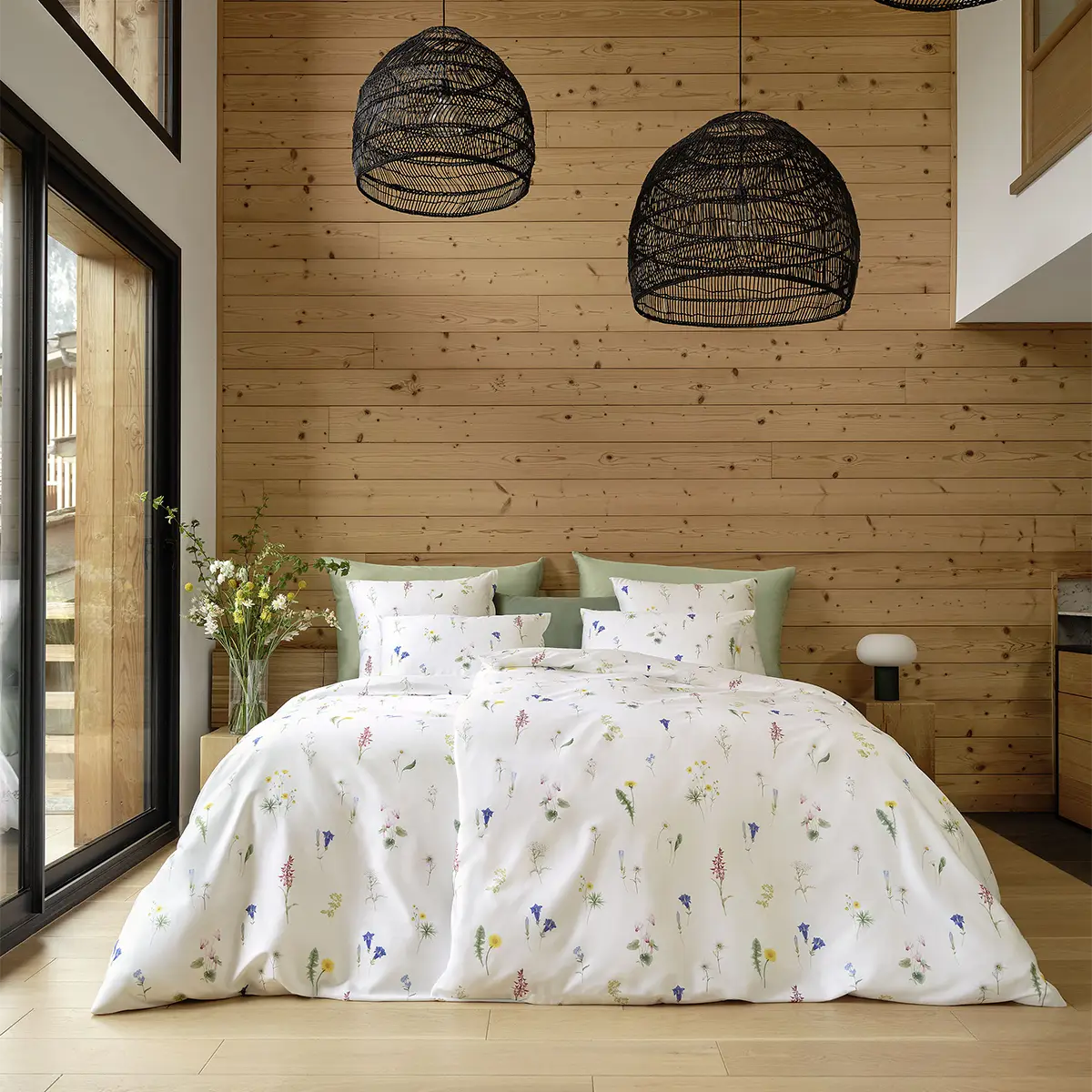 Ein gemütliches Schlafzimmer mit Holzverkleidung, dekoriert mit der weissen Bettwäsche "Flurina", die mit einem zarten Blumenmuster verziert ist.
