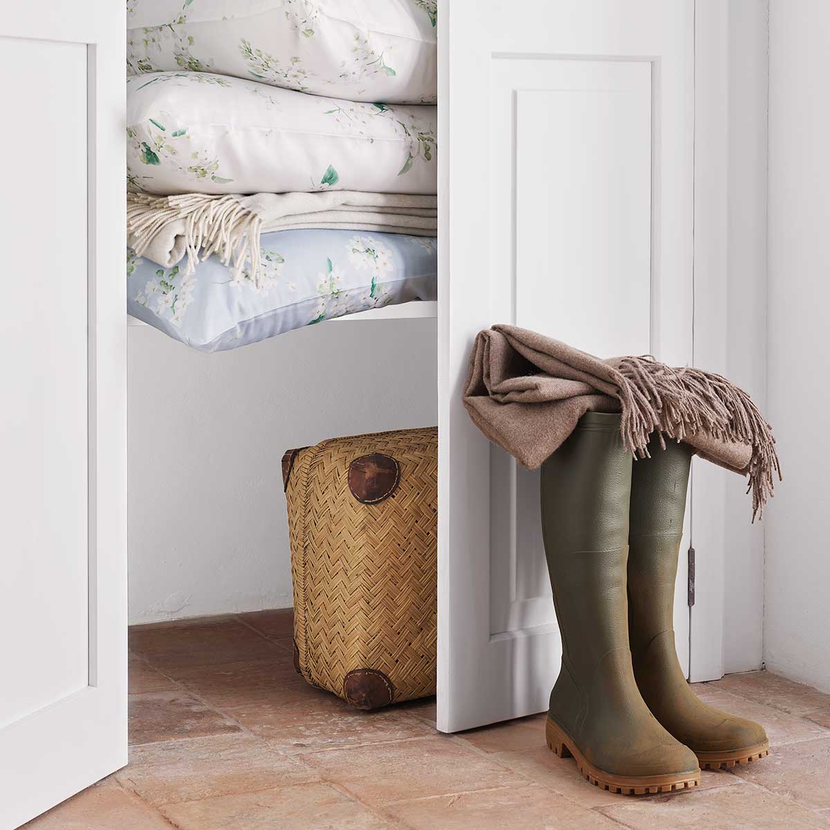 Gestapelte Bettwäsche May im Schrank Gestapelte Bettwäsche May mit floralem Muster in einem Schrank, kombiniert mit anderen Textilien und dekorativen Elementen.