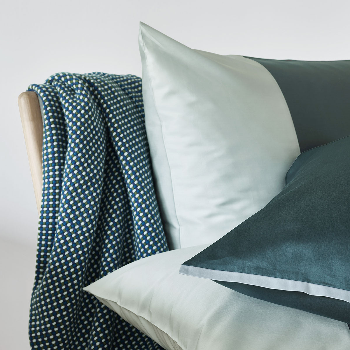 Nahaufnahme von weissen und dunkelgrünen Kissen, die auf einem Stuhl mit einer blau-weiss gemusterten Decke liegen.