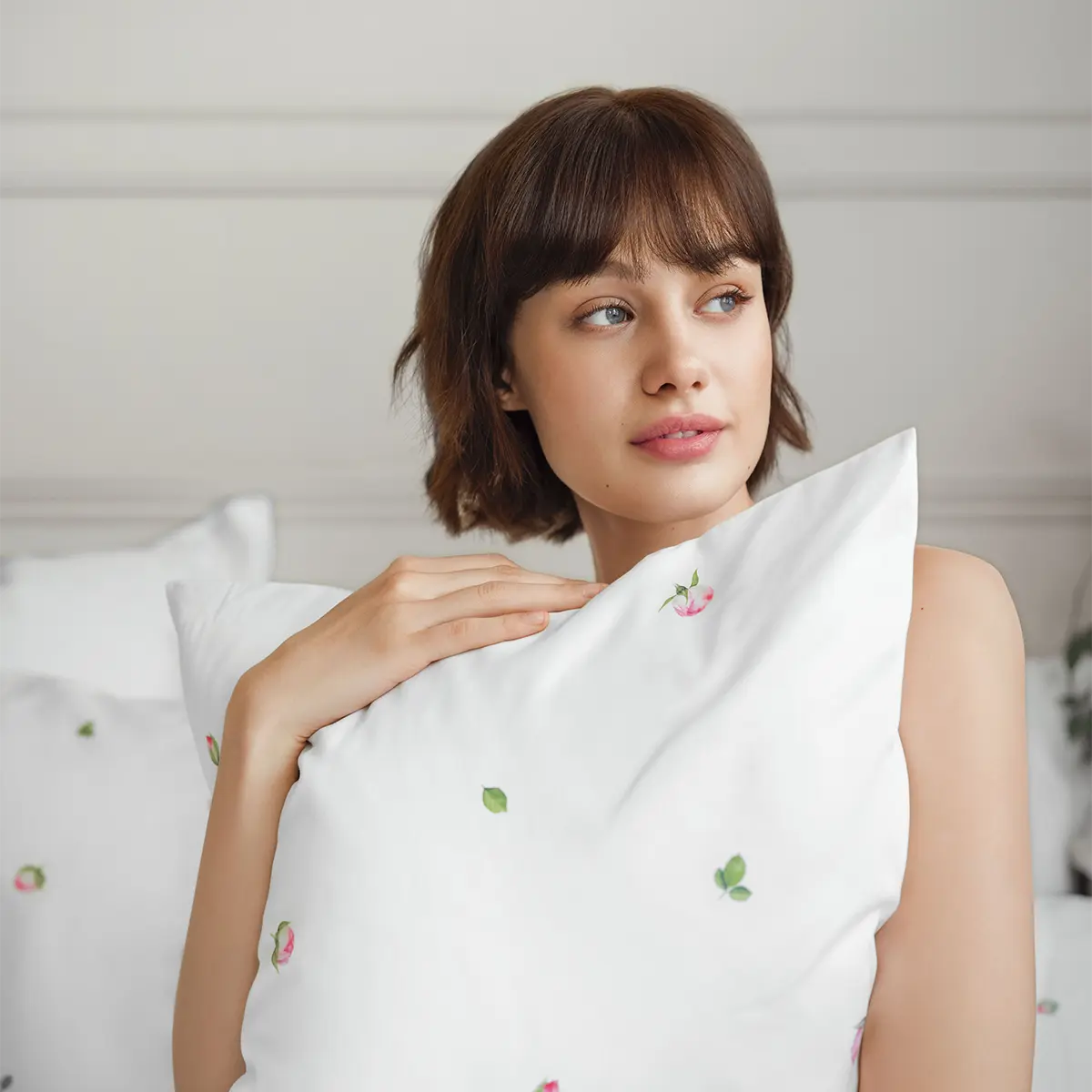 Eine Frau kuschelt sich in die Jeunesse-Bettwäsche, die mit zarten rosa Blüten verziert ist, und geniesst einen ruhigen Moment.