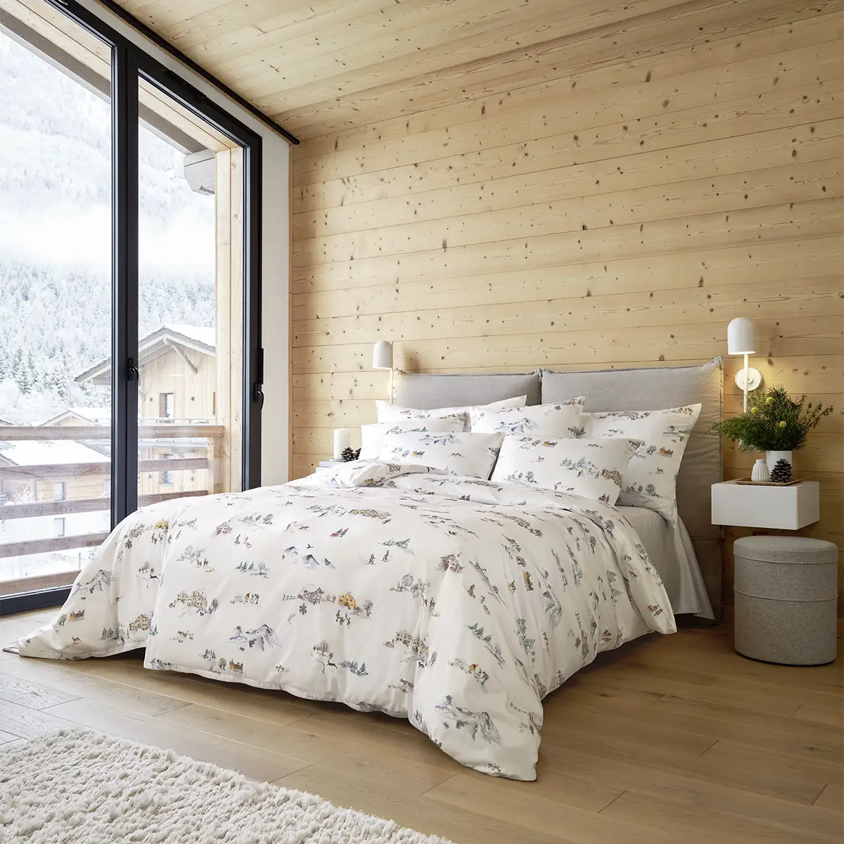 Alpines Schlafzimmer mit Montagne Bettwäsche Schlafzimmer mit einer grossen Fensterfront und der Montagne Bettwäsche, die eine winterliche Berglandschaft darstellt.