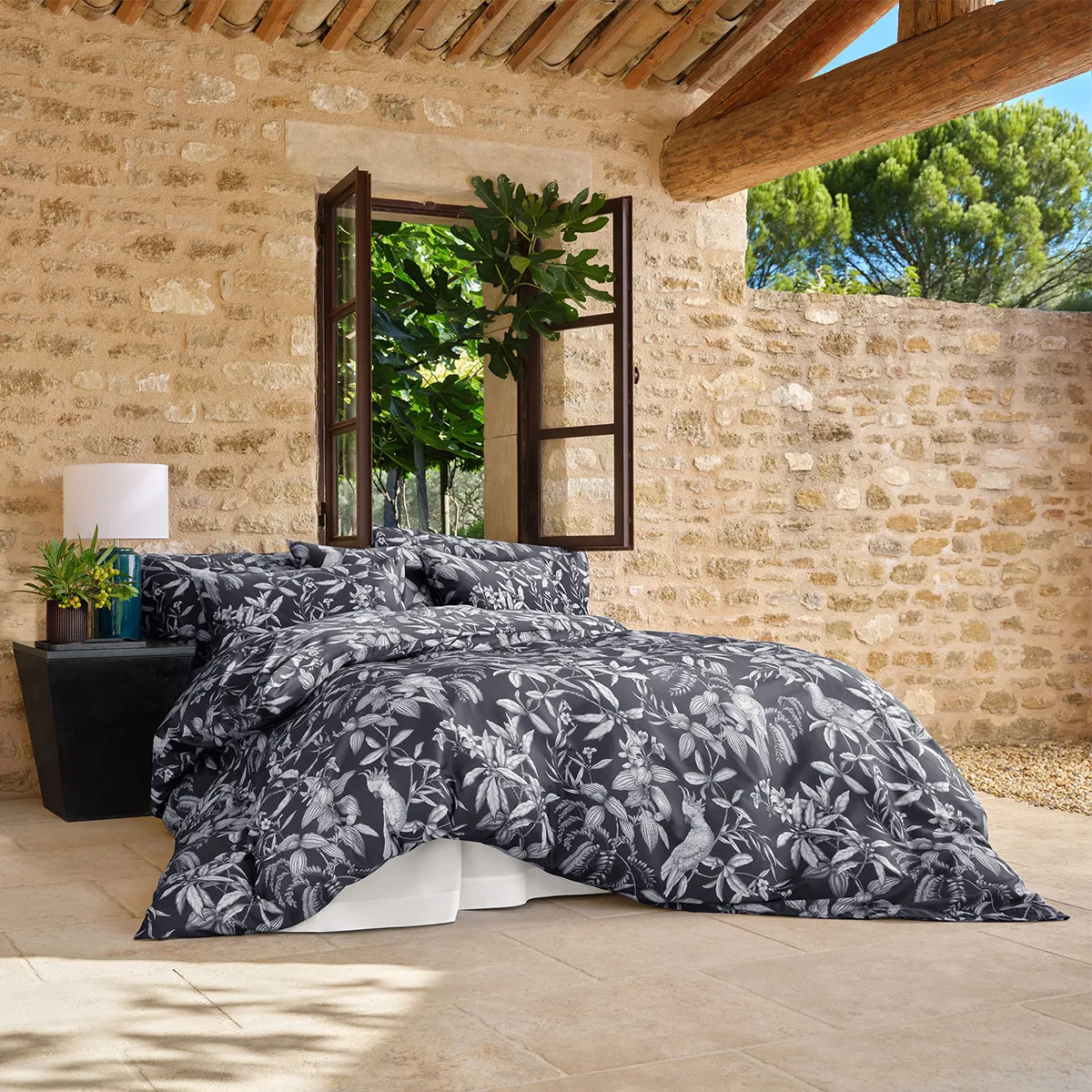 Schlossberg Bettwäsche Calypso Noir – Hero Ansicht Blick auf das Schlafzimmer mit der Schlossberg Bettwäsche Calypso Noir, die ein elegantes, botanisches Design auf einem dunkelgrauen Hintergrund zeigt.