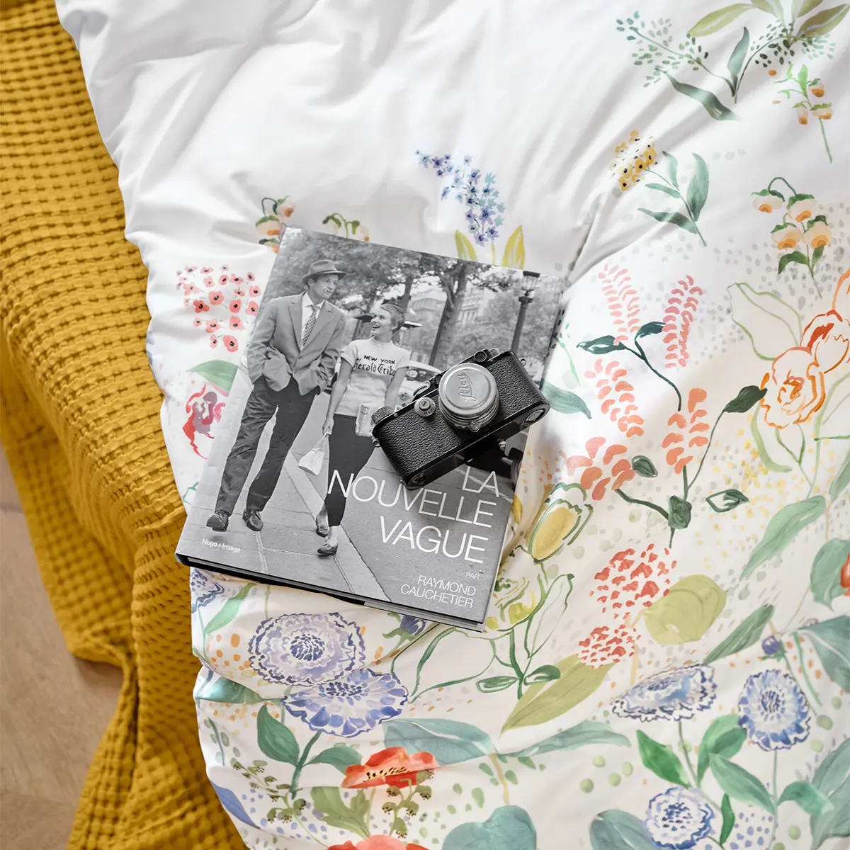 Nahaufnahme der Bettwäsche Annika mit floralem Muster, darauf liegen ein Buch und eine Kamera.