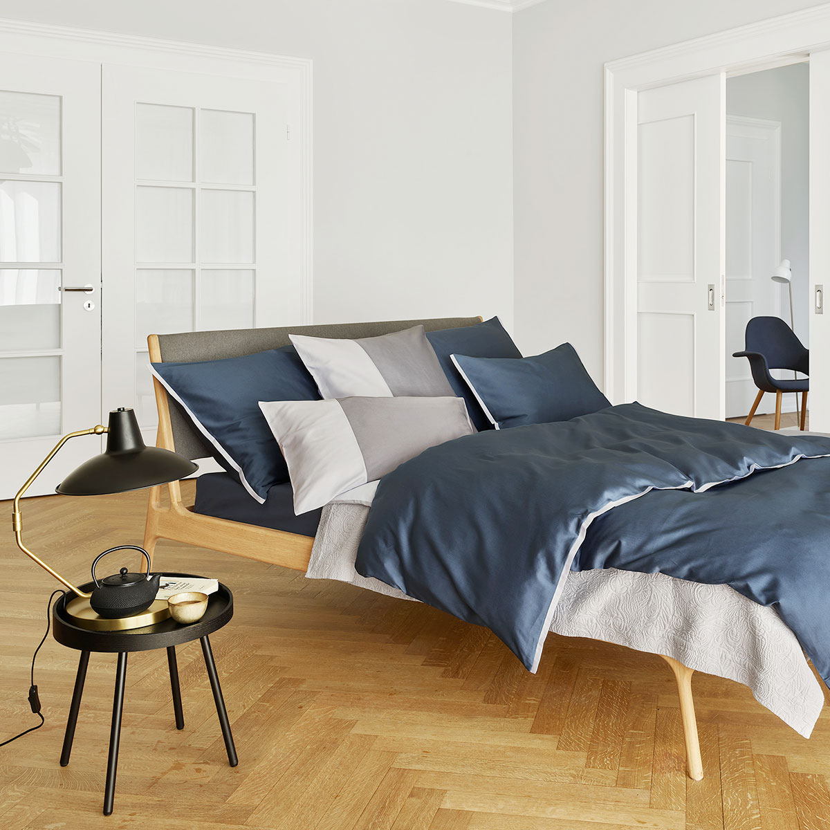 Ein elegantes Schlafzimmer mit einem Bett, das mit der dunkelblauen und weissen Bettwäsche Clark bezogen ist. Ein stylischer Nachttisch und Accessoires ergänzen das Ambiente.