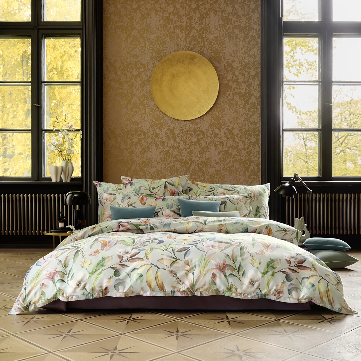 Schlossberg Bettwäsche Adele Schlafzimmer Ein Schlafzimmer mit Schlossberg Bettwäsche im Adele Design, das florale Muster in sanften Farben zeigt. Kissen in verschiedenen Größen und Farben sind auf dem Bett arrangiert, vor einem großen Fenster mit Herbstblick.