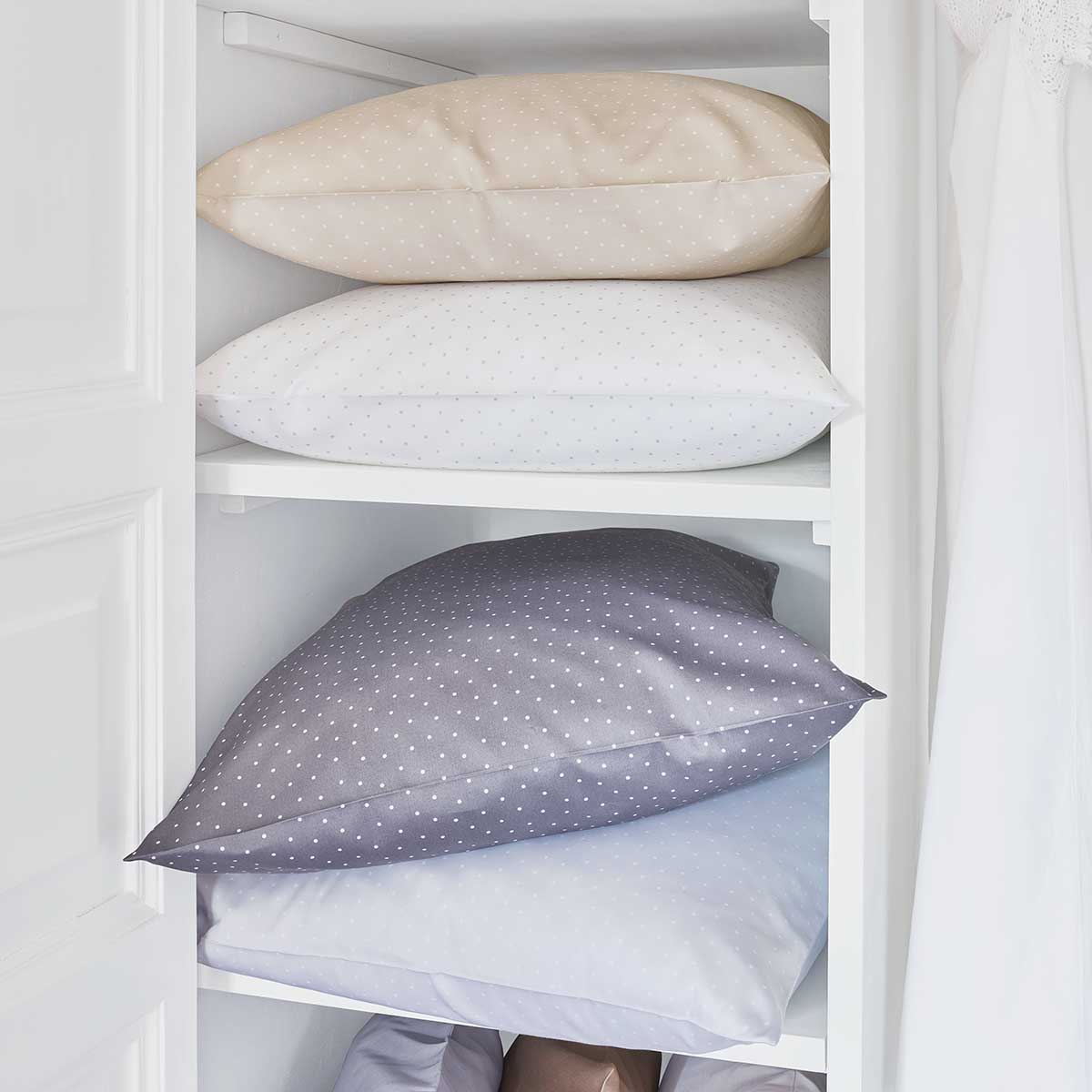 Gestapelte Kissen der Bettwäsche Emily in verschiedenen Farben (Beige, Weiss, Grau) in einem Regal.