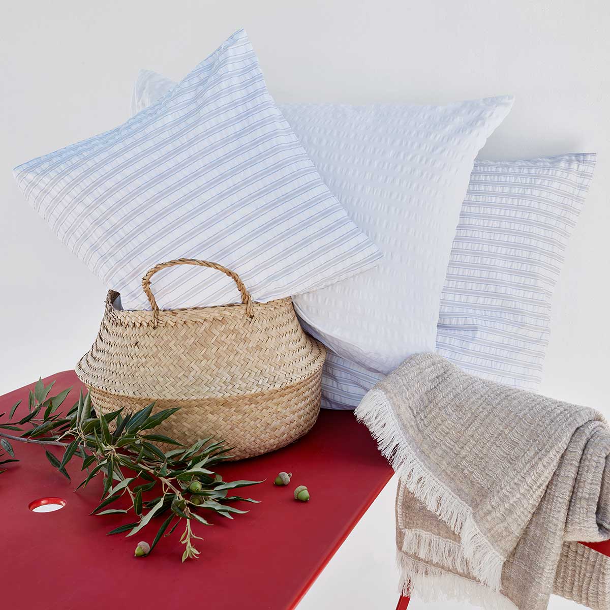 Dekorative Kissen der Bettwäsche Dean Bettwäsche Dean, in Weiss und blau-weiss gestreift, zusammen mit einem geflochtenen Korb und einer Decke auf einem roten Tisch arrangiert.