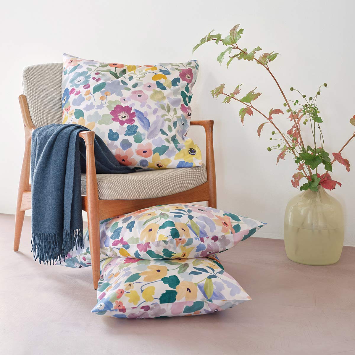Dekorative Kissen auf einem Stuhl mit Bettwäsche "Hanna" Kissen in der Bettwäsche "Hanna" mit buntem Blumenmuster, dekorativ auf einem Stuhl arrangiert.